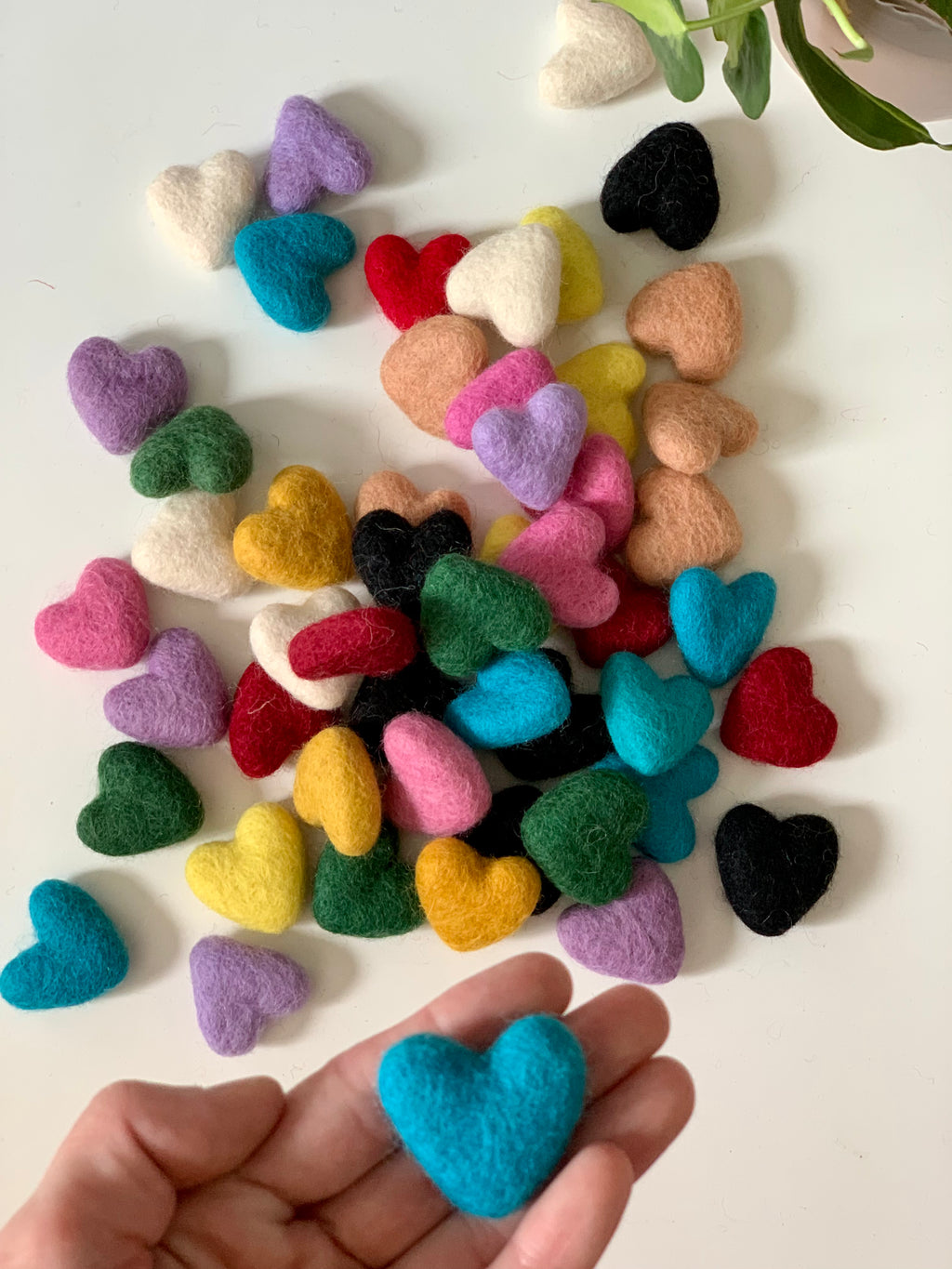 Colorful small handmade felt hearts in various colors scattered on white surface with one held in hand