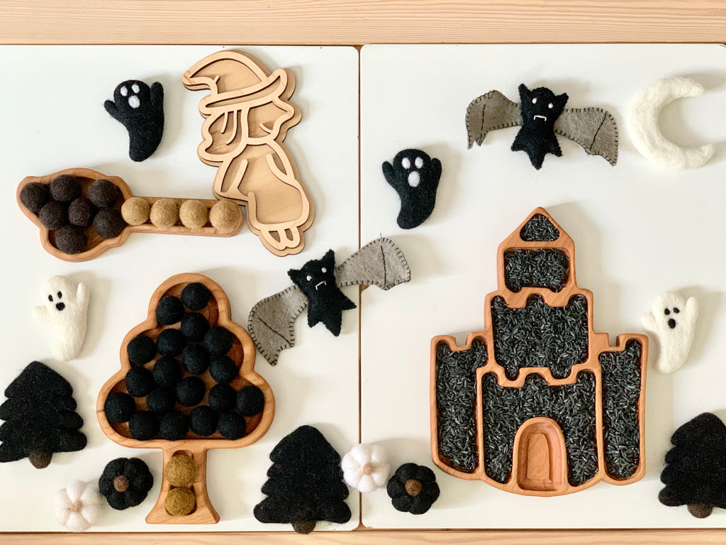 Fillable witch play tray with wooden witch cookie cutter, felt bats, ghosts, black pom poms, and castle-shaped tray on white surface
