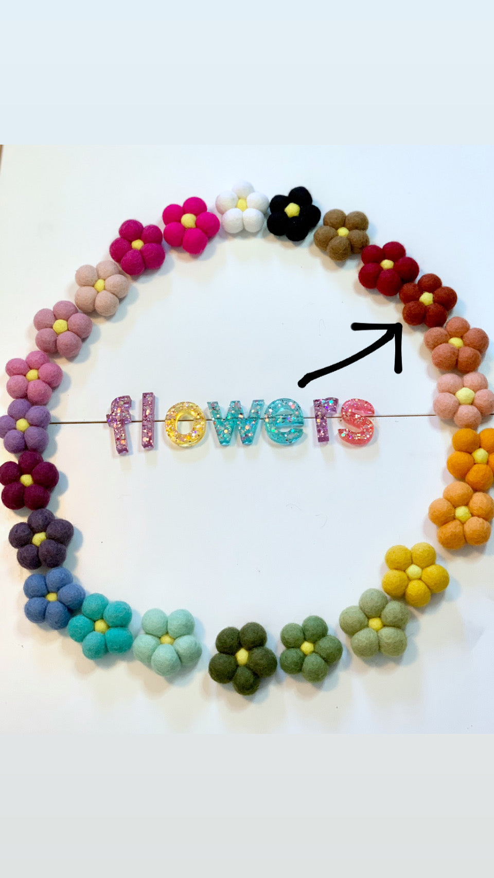 Colorful handmade felt flowers arranged in a circle with glitter letters spelling flowers on white background