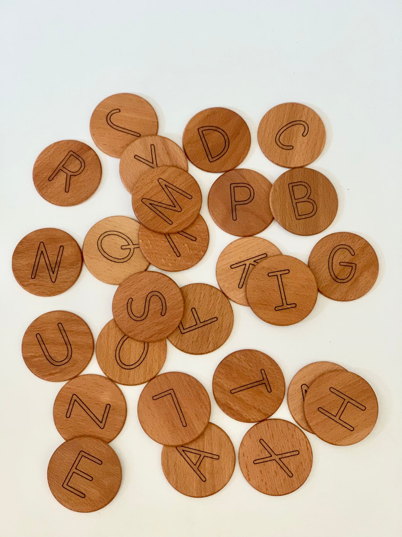 Natural wooden alphabet discs engraved with capital letters scattered on white background for learning and play