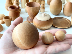 Hand holding three smooth unfinished wooden balls of varying sizes with assorted wooden shapes in the background