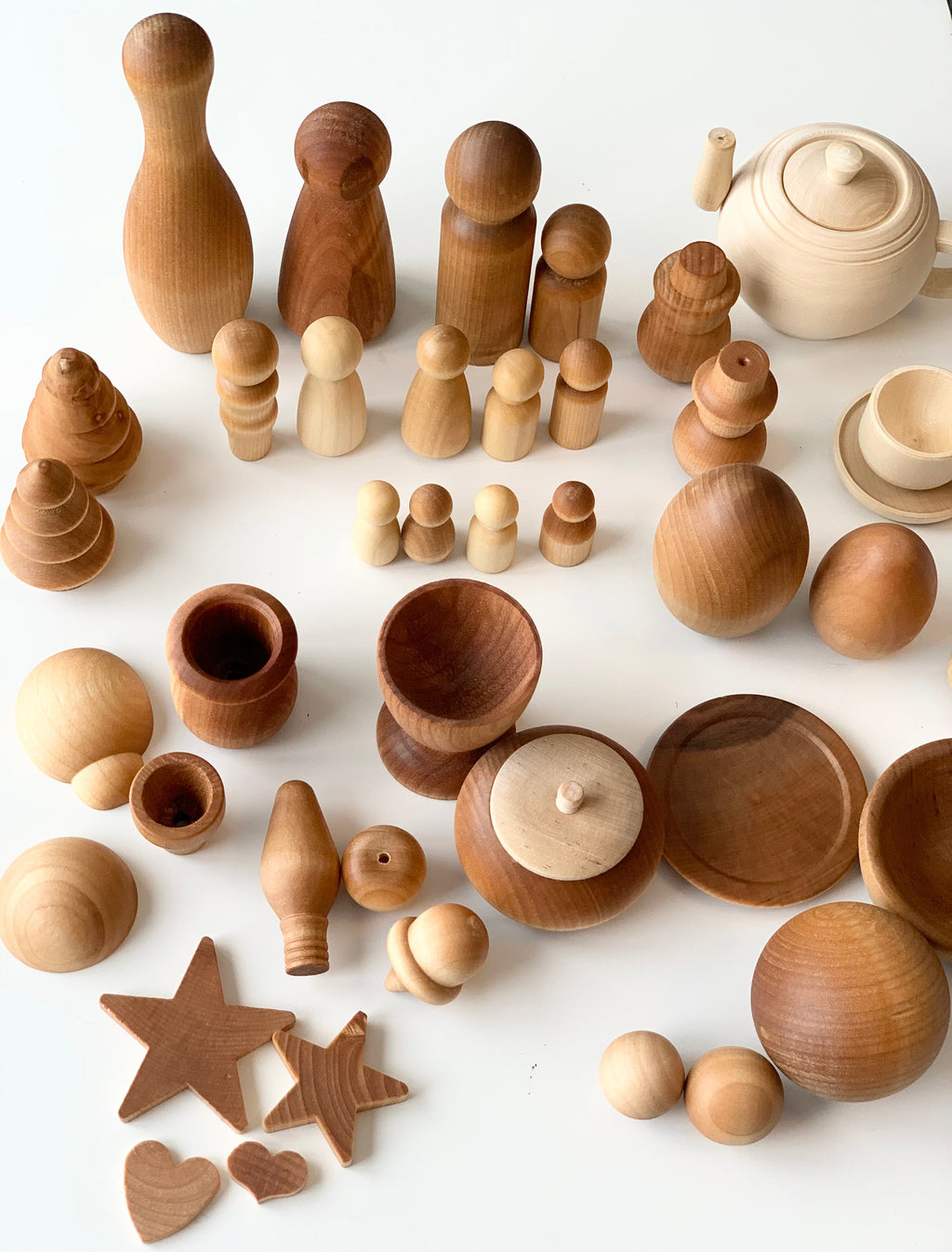 Assorted unfinished wooden figurines, bowls, cups, teapot, stars, hearts, and abstract shapes on a white surface