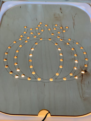 Wooden Flisat insert shaped like a pumpkin with small circular holes lit from underneath on light wood surface