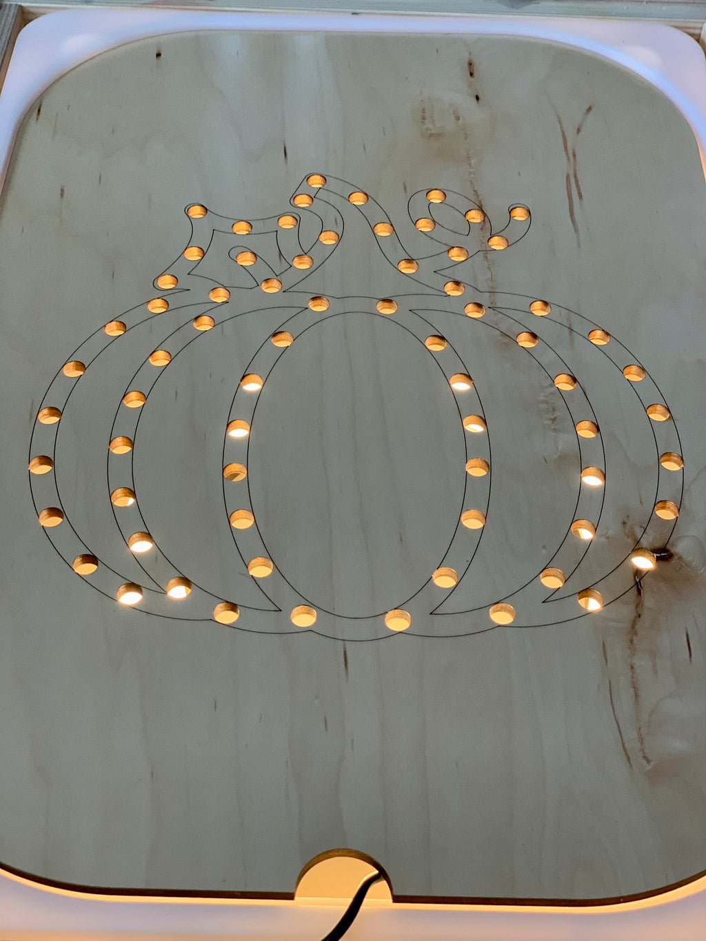 Wooden Flisat insert shaped like a pumpkin with small circular holes lit from underneath on light wood surface
