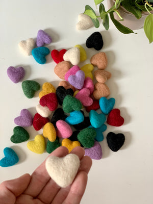 Small handmade felt heart in cream color held in hand with scattered colorful felt hearts on white background