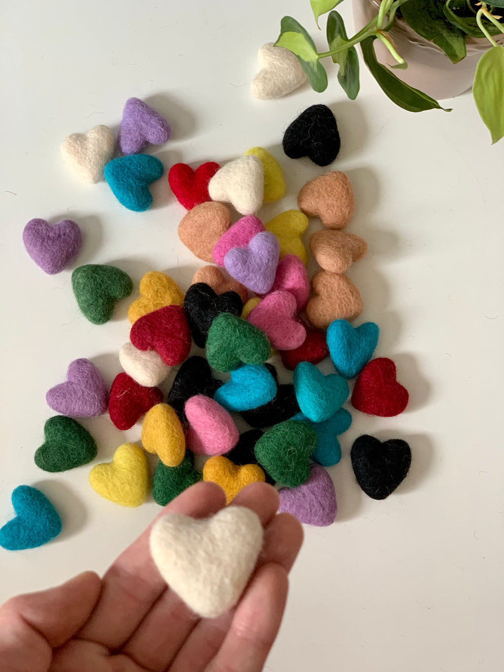 Small handmade felt heart in cream color held in hand with scattered colorful felt hearts on white background