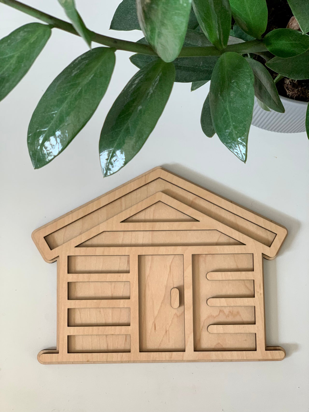 Maple wood fillable log home play tray with carved door and log details on white surface with green plant leaves above