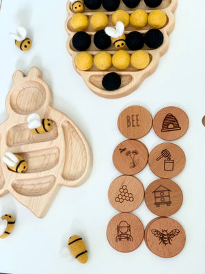 Bee themed memory game with wooden tokens engraved with bee illustrations and felt bee playing pieces on white background