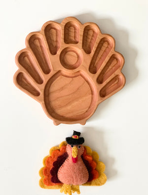 Wooden turkey-shaped sensory tray with multiple compartments and a felt turkey toy on white background