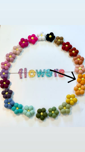 Circle of colorful handmade felt flowers arranged around glittery letters spelling flowers on white background