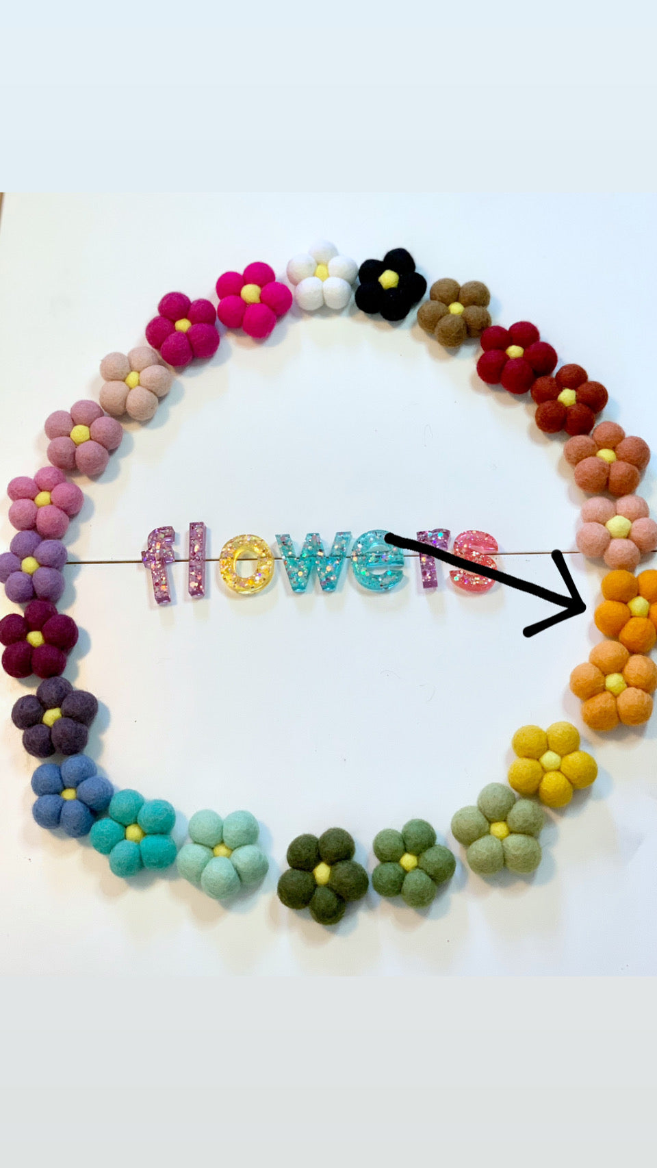 Circle of colorful handmade felt flowers arranged around glittery letters spelling flowers on white background