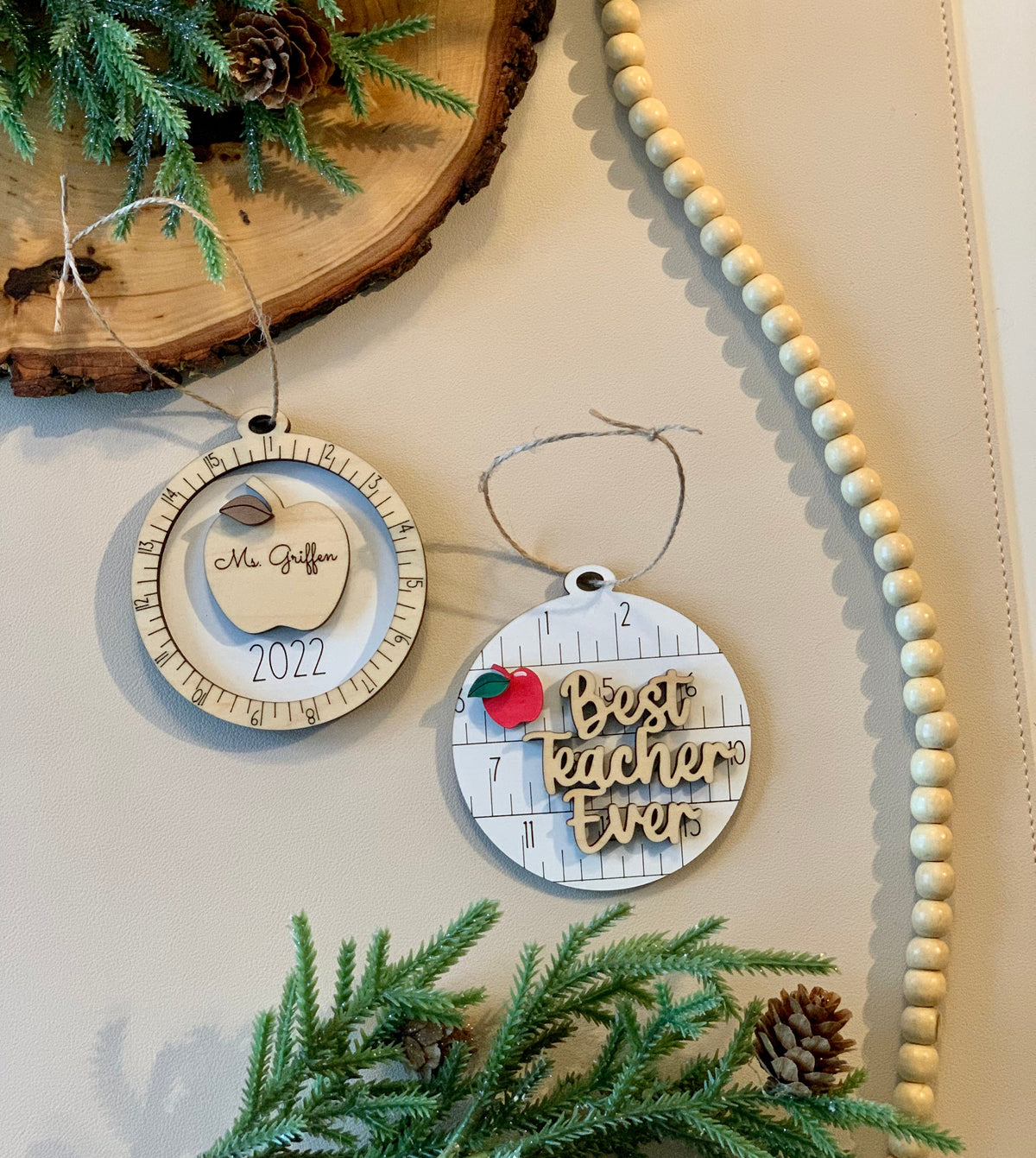 Two round wooden teacher Christmas ornaments with engraved apple and "Best teacher ever" text on light background