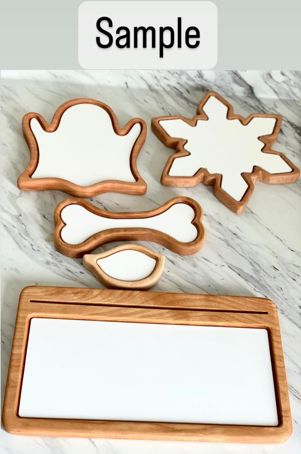 Set of wooden sensory trays with white insert shapes including ghost, snowflake, bone, bird, and rectangular tray on marble surface