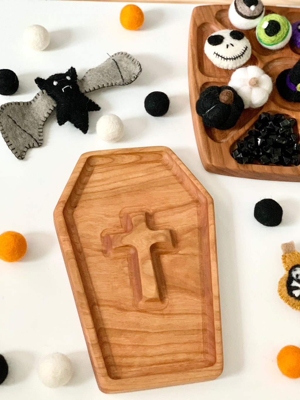 Wooden coffin-shaped sensory tray with carved cross detail surrounded by felt balls and Halloween-themed decorations
