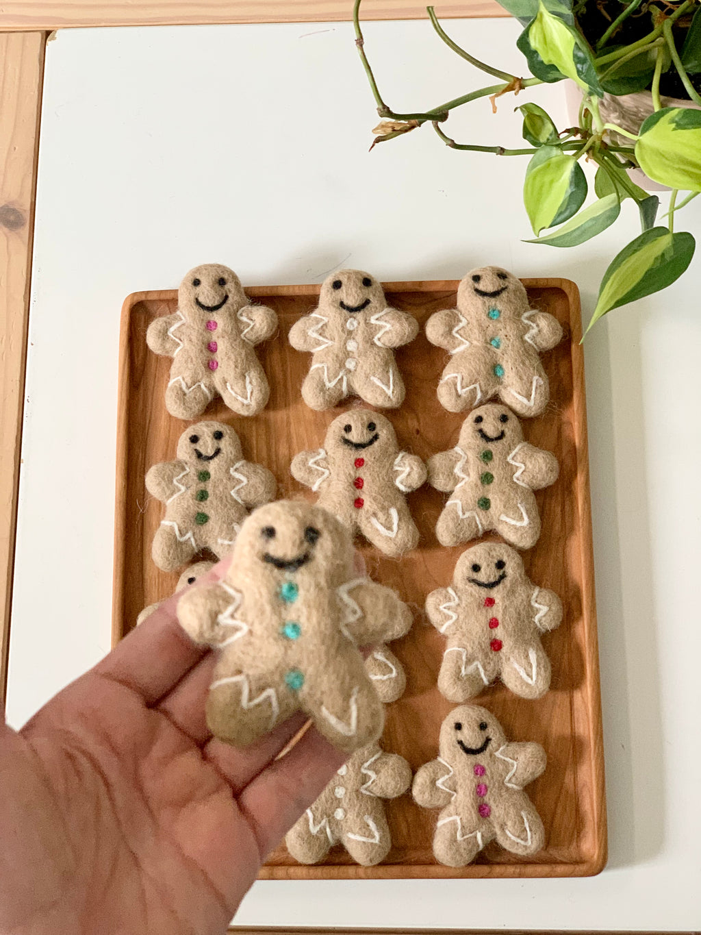 Handmade felt gingerbread person with colorful buttons and white icing details held above tray of similar figures on wooden tray