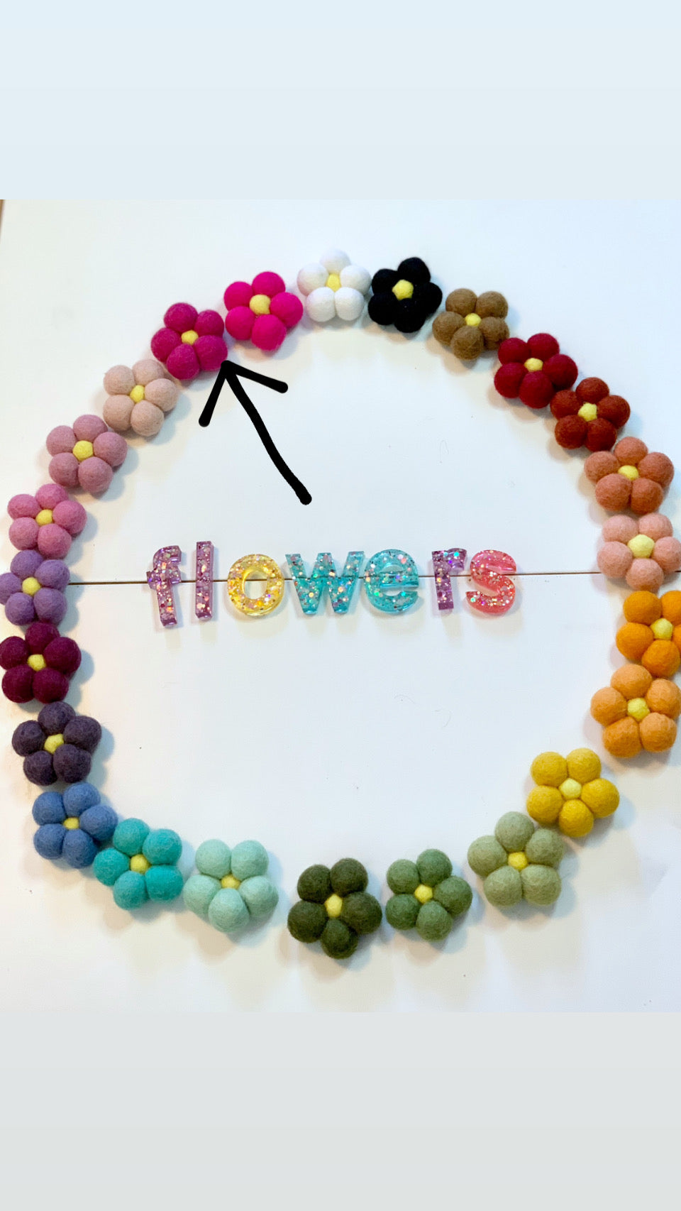 Single bright pink felt flower with yellow center among multicolored handmade wool felt flowers on white background