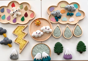 Wooden trays shaped like clouds, raindrops, and lightning holding colorful felt weather-themed pieces and textured materials