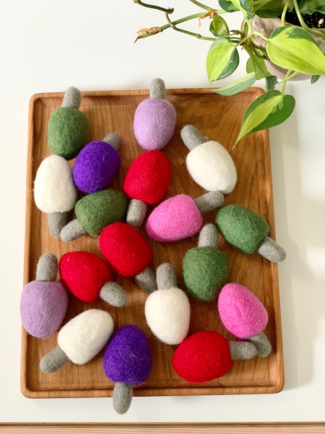 Wooden tray filled with colorful handmade felt lightbulbs in red, purple, green, pink, and white on white table with plant nearby