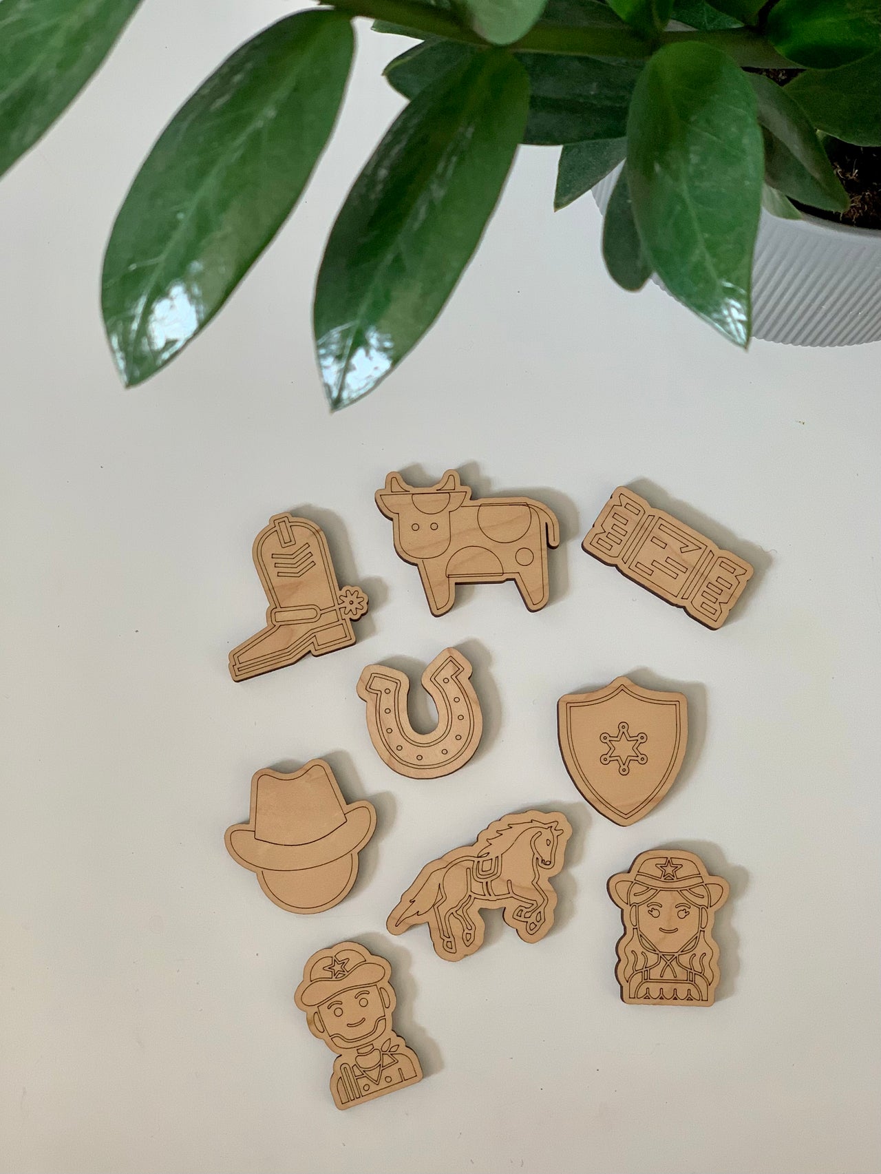 Laser-cut wooden western themed loose parts including cowboy hat, horse, sheriff badge, boots, cow, horseshoe, ticket, and character faces on white surface