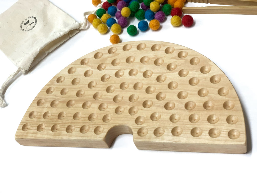Half-circle natural wood sorting board with smooth engraved holes and colorful felt balls on white surface