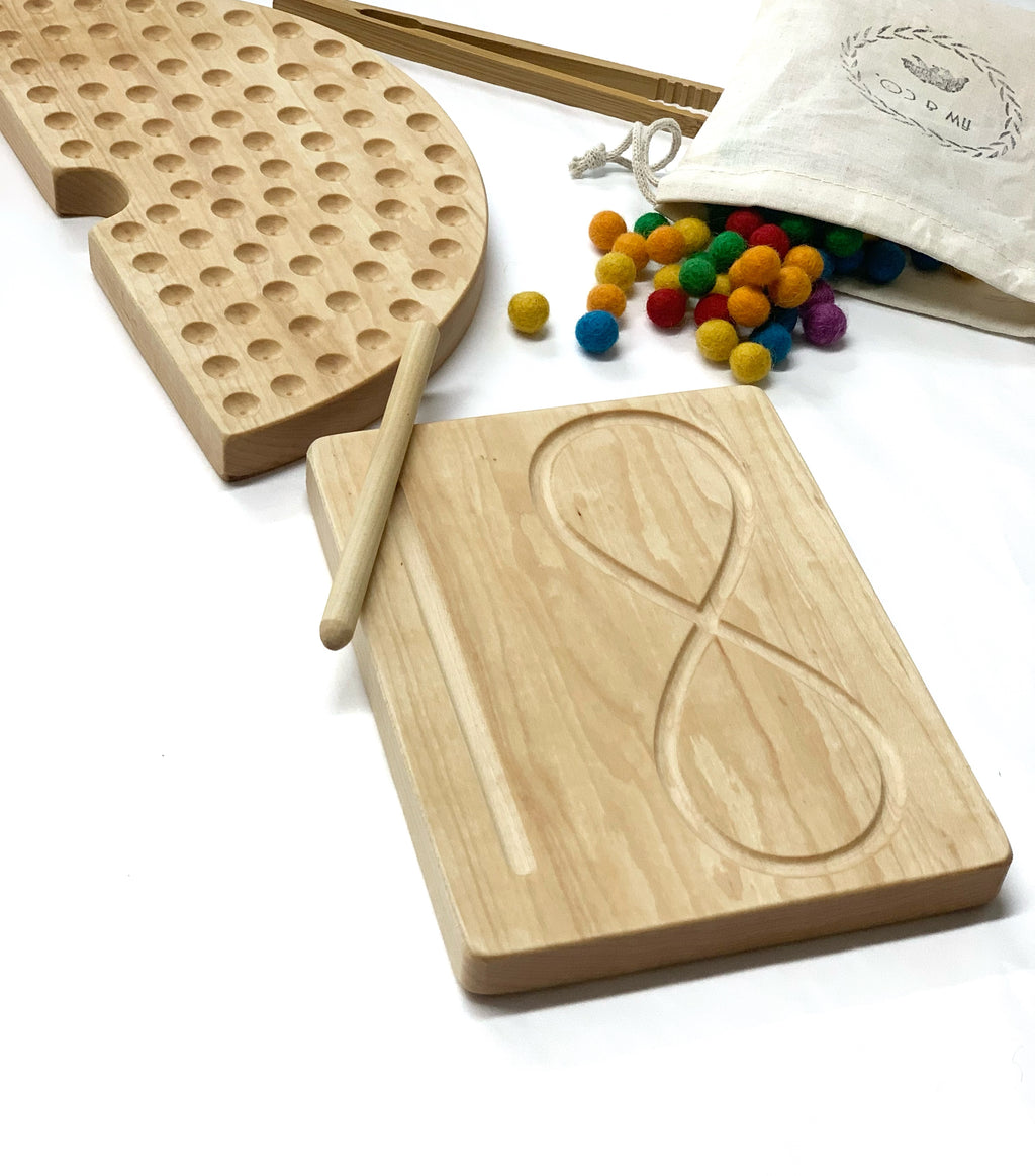 Light natural maple wooden infinity figure eight tracing board with stylus surrounded by colorful felt balls and wooden pegboard on white background