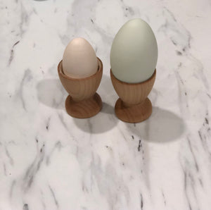 Two natural wood eggs in neutral tones placed in small wooden egg cups on a marble surface for Montessori play.