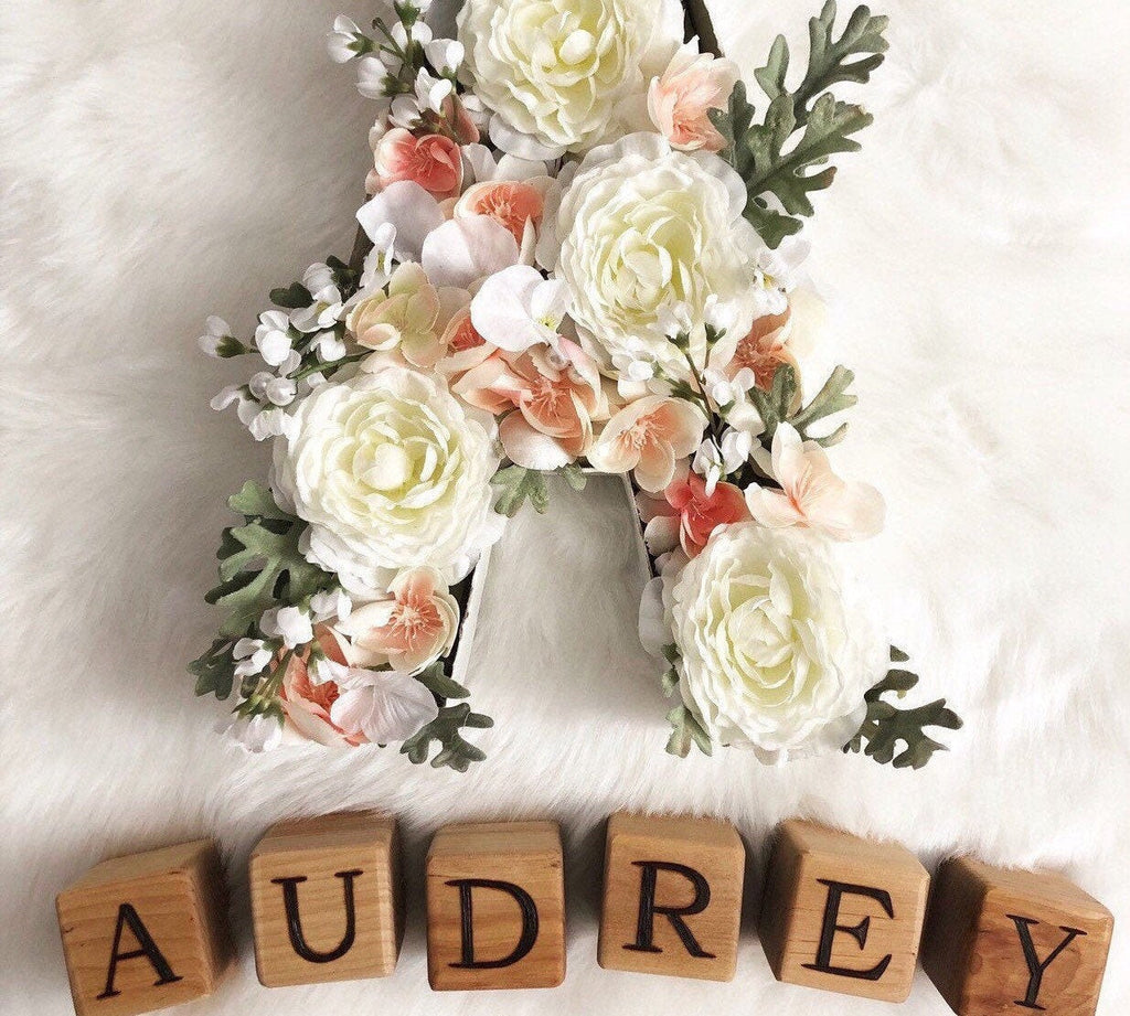 Custom wood blocks spelling AUDREY with floral decorated letter A on white fur background