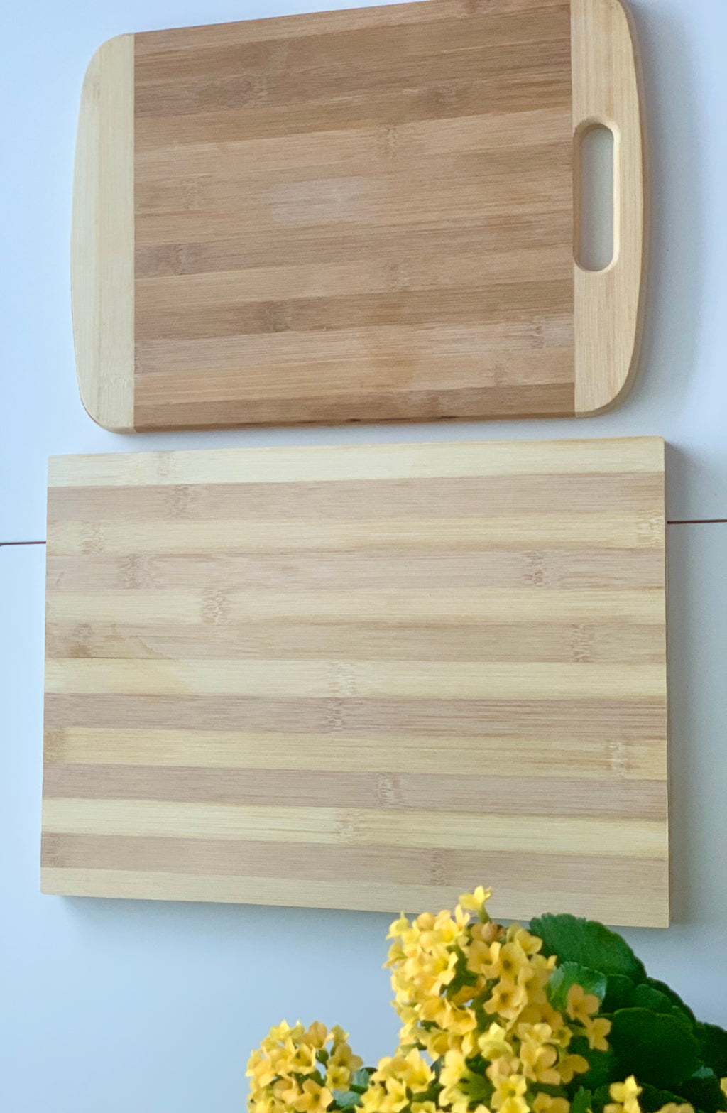 Two natural bamboo cutting and serving boards with striped patterns and a yellow flowering plant on white surface
