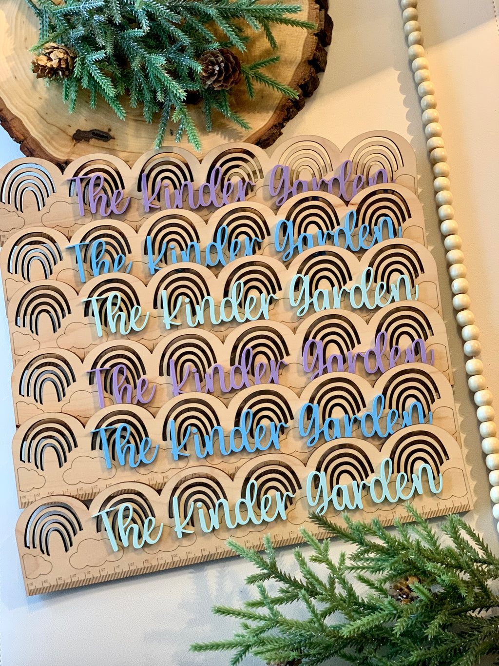 Personalized wooden rainbow rulers with engraved black rainbows and handwritten style text in pastel colors on natural wood background
