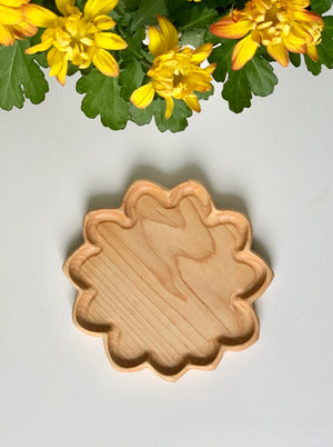 Natural light wooden flower-shaped sensory tray with smooth edges on white surface surrounded by yellow flowers