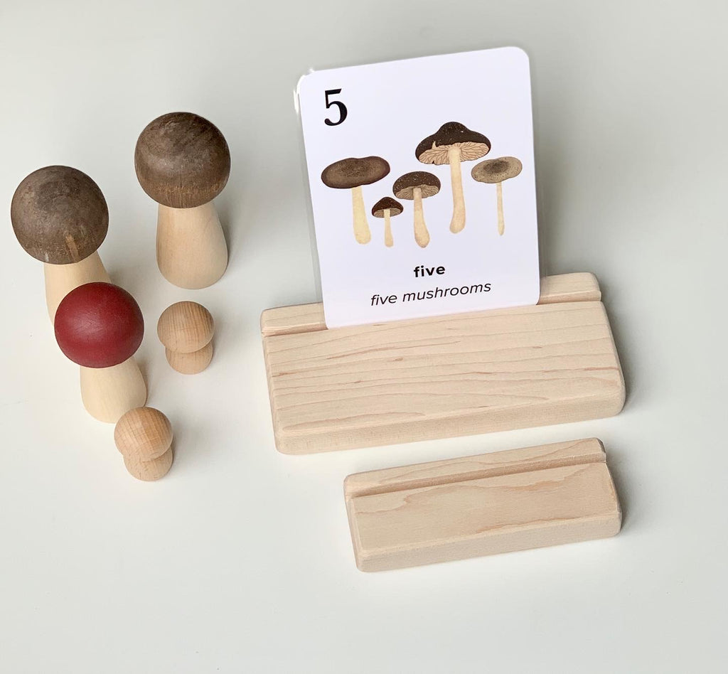 Natural wooden flash card holder with a mushroom counting flash card and wooden peg toys on white background