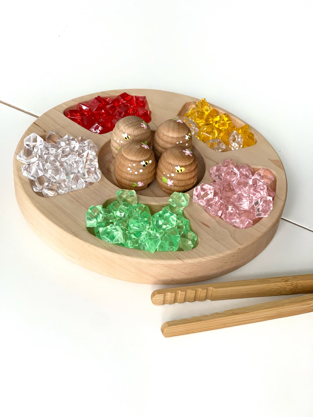 Round wooden circular tinker tray with five compartments filled with colorful transparent gem pieces and wooden bees in center