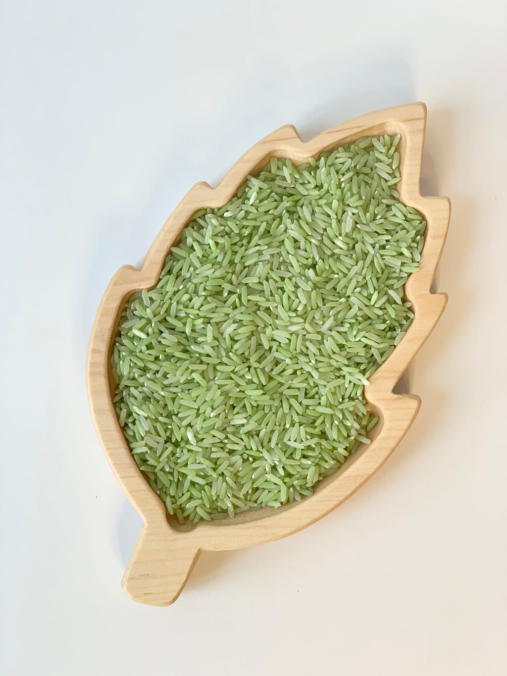 Natural birch wood leaf-shaped sensory tray filled with green rice on white background