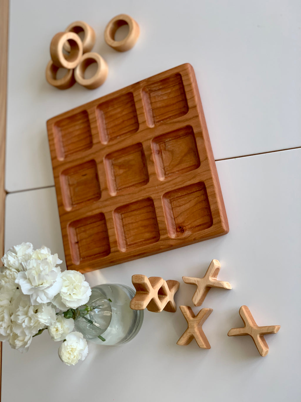 Natural cherry wood tic tac toe board with nine square frames and round and X game pieces on white table