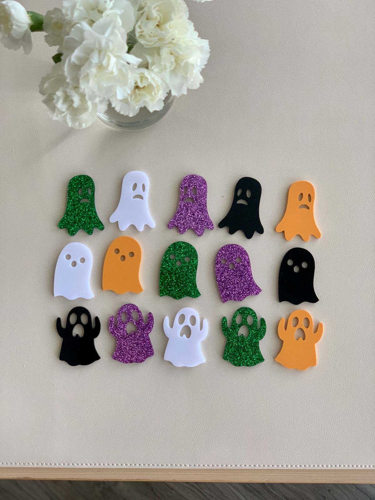 Set of colorful Halloween ghost acrylic shapes in green, white, purple, black, and orange arranged on beige surface