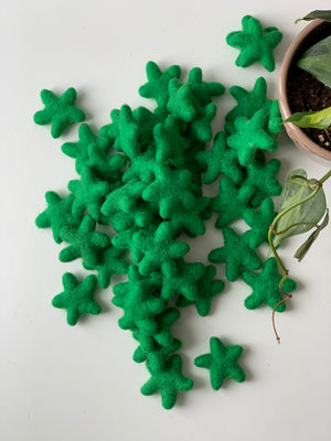 Small handmade green felt stars made from pure New Zealand wool scattered on white surface near plant pot