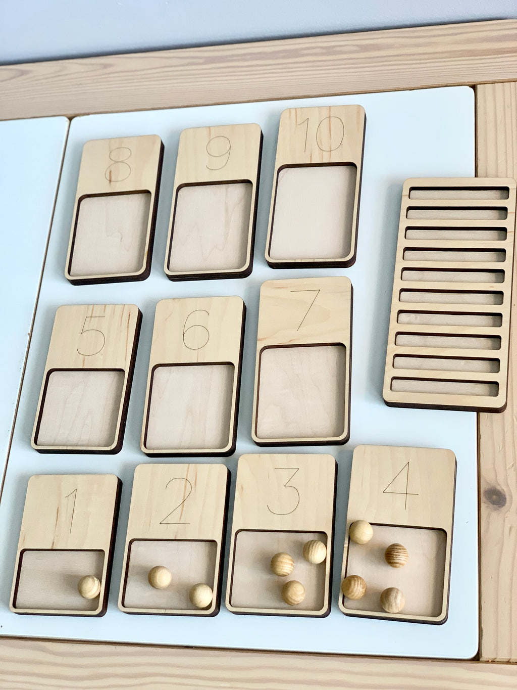 Wooden 1-10 counting trays with engraved numbers and round wooden counters on a white base with wooden stand nearby