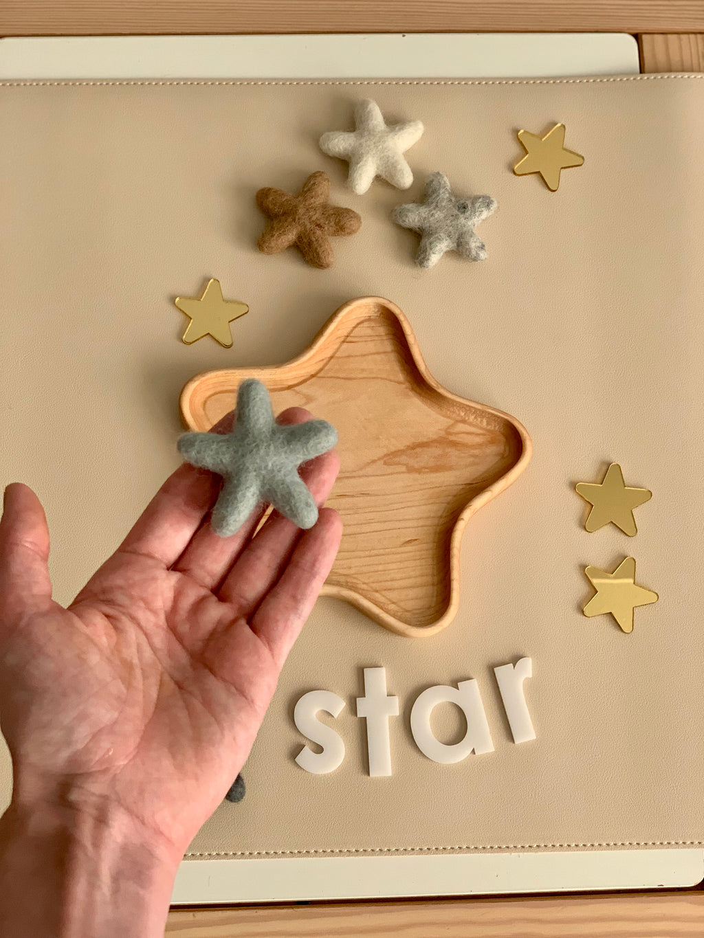 Hand holding gray felt star above wooden star-shaped tray with other neutral felt stars and white letters spelling star