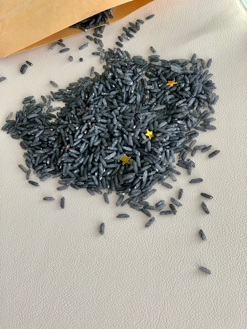 Black dyed rice sensory bin filler with scattered gold star confetti on textured neutral background