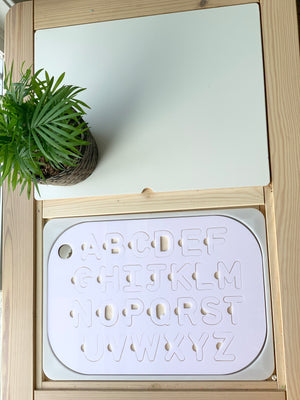 Maple wood Flisat table top insert with white acrylic uppercase alphabet puzzle pieces inside wooden frame with green plant nearby