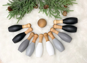 Monochrome wood bowling set with 10 pieces arranged on white fur background with green pine and pinecones above