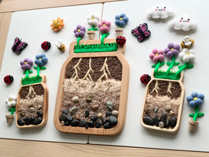 Three large wooden jar plate sensory trays filled with natural materials and decorated with felt flowers and insects on white surface