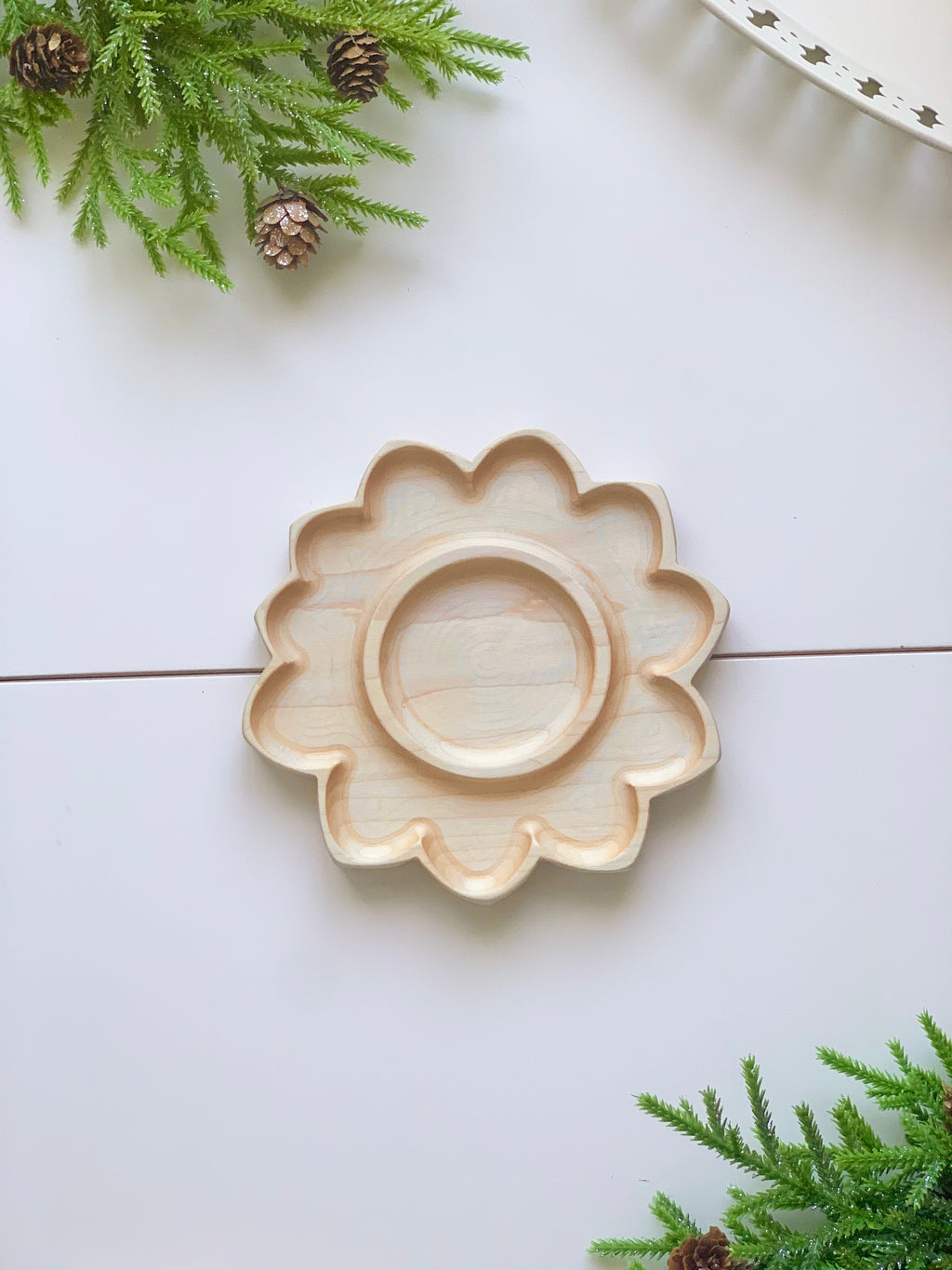 Natural wooden sunflower-shaped sensory tray with smooth carved petals on white surface with pine branches