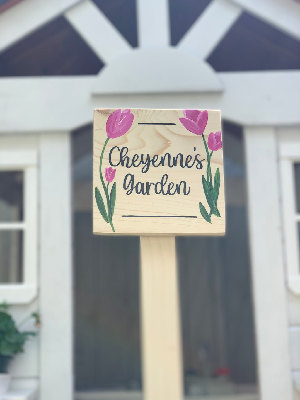 Small natural wooden square garden sign with pink tulip illustrations and black cursive lettering on stake outdoors