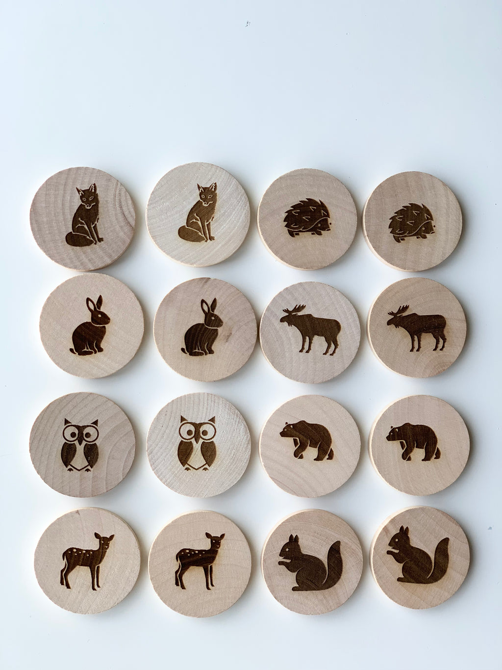 Natural wooden memory game discs with engraved woodland animals including fox, hedgehog, rabbit, moose, owl, bear, deer, and squirrel on white background