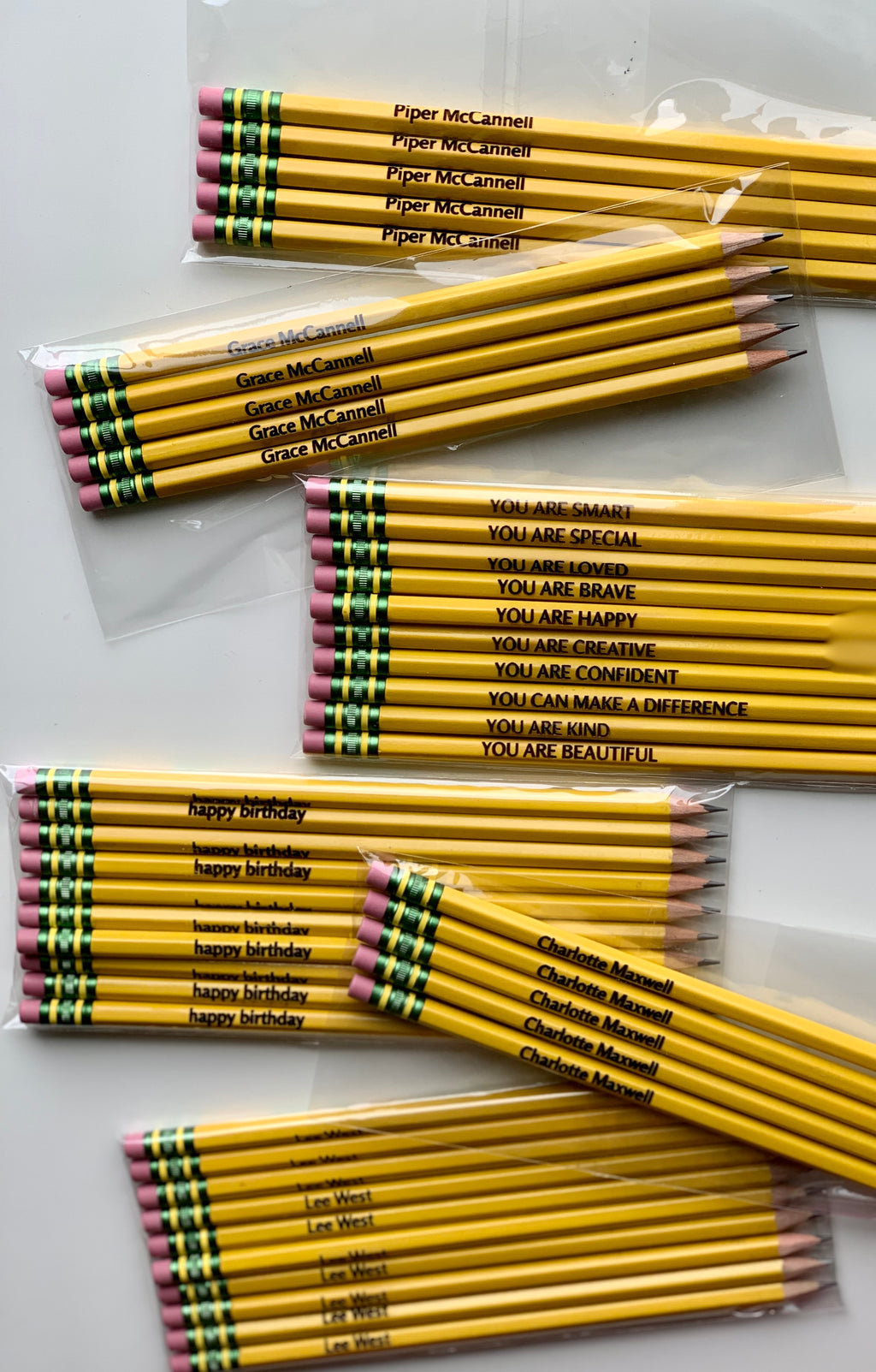 Bundles of yellow personalized pencils with custom names and positive messages, each pencil sharpened with pink erasers