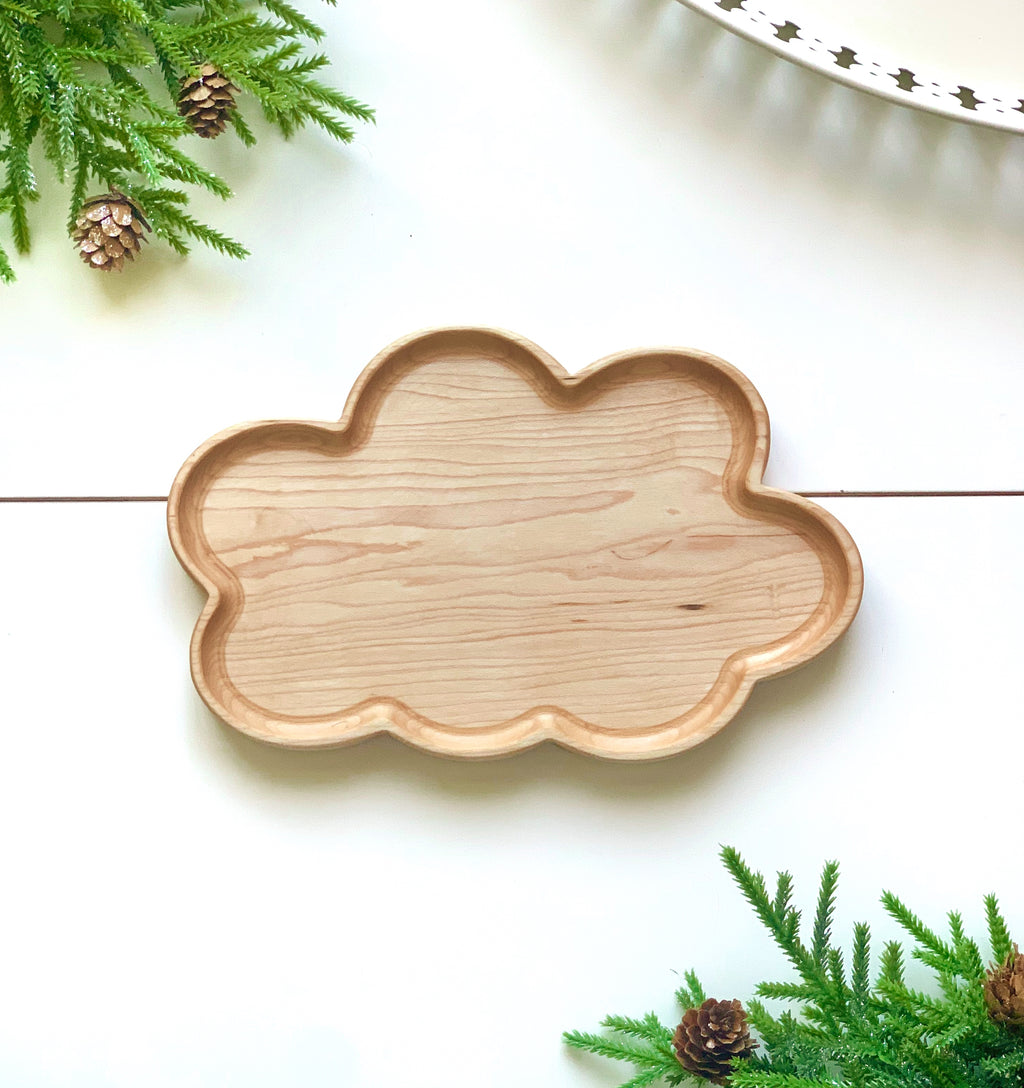 Natural wooden cloud-shaped sensory tray with smooth finish on white surface surrounded by green pine branches with cones