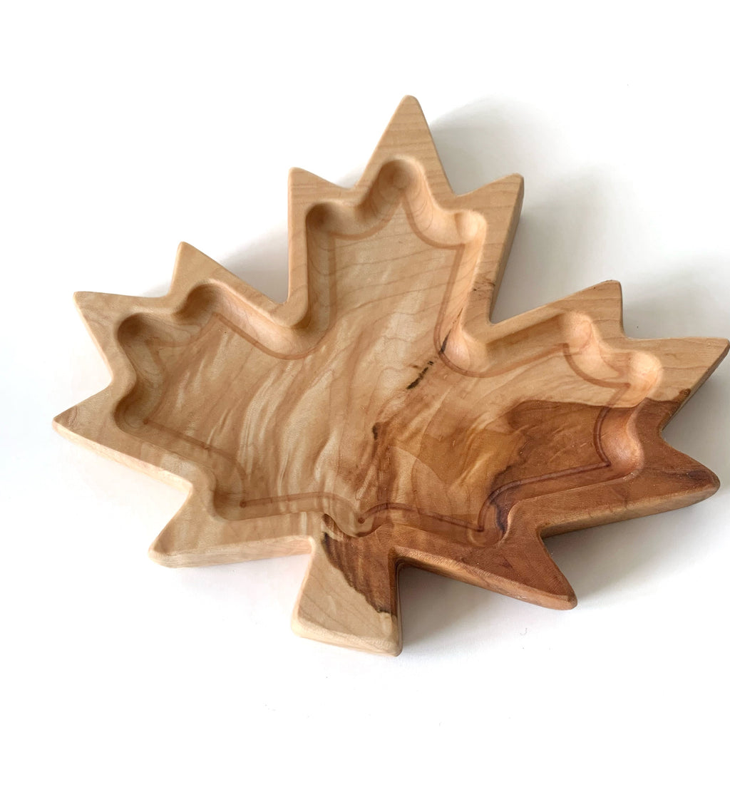 Maple leaf-shaped wooden plate with natural wood grain patterns and carved shallow sections on white background