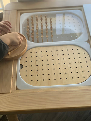 Wooden small hole peg board with geometric light board inserts and wooden pegs on natural wood table with child’s hands