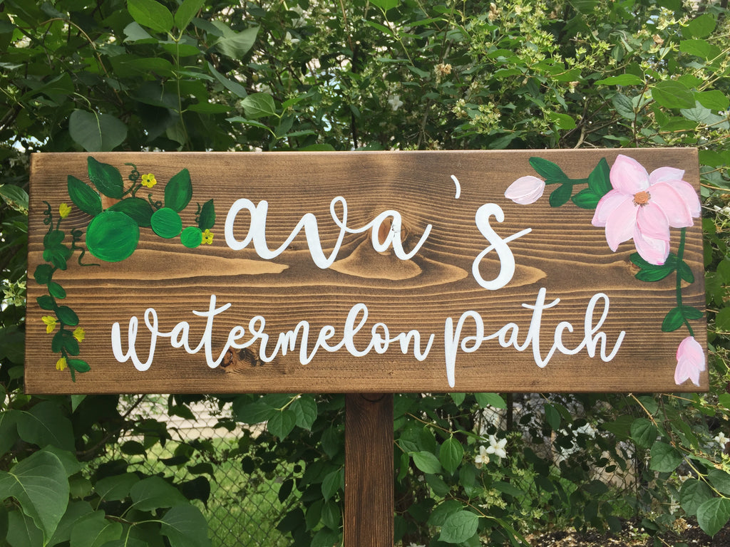 Large personalized wooden garden sign with white cursive letters and hand-painted floral and watermelon illustrations on natural wood background